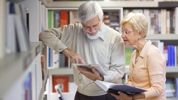 Seniors couple in the library using digital tablet, e-reader