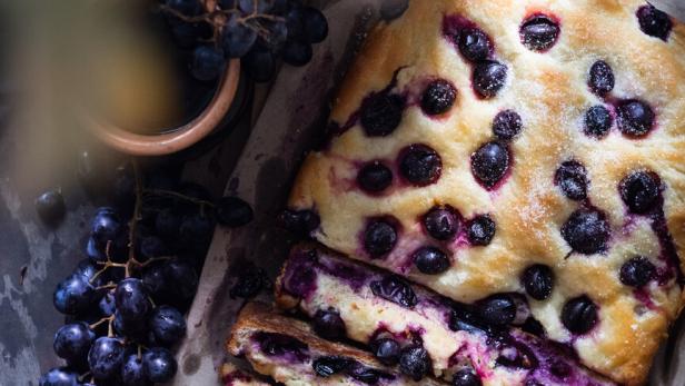 Ein angeschnittenes Traubenbrot liegt neben frischen Trauben auf einem Holztisch.