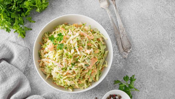 Ein Schüssel Krautsalat mit Karotten und Petersilie auf einem grauen Tisch.