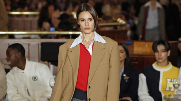 Eine Frau präsentiert einen beigen Blazer und einen Faltenrock von Tommy Hilfiger.