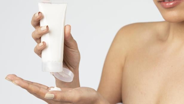 Frau versucht Bodylotion aus einer Tube zu drücken.