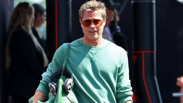 Brad Pitt mit Sonnenbrille, Jeans und grüner Tasche bei einem Formel-1-Rennen.
