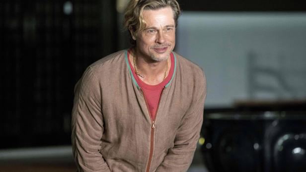 Brad Pitt lächelt in einem braunen Cardigan und einer goldenen Halskette.
