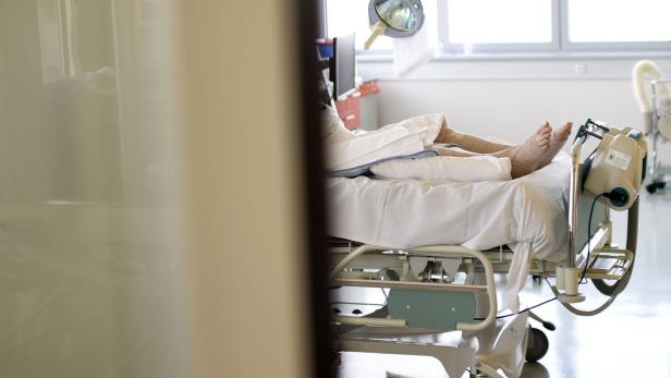 Eine Person liegt mit bandagierten Beinen in einem Krankenhausbett.