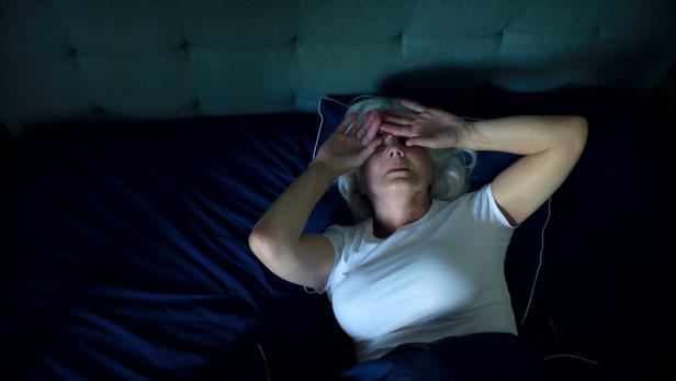 Eine Frau liegt im Bett im Dunkeln und hält sich die Augen zu.