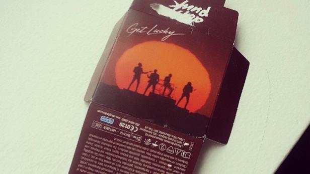 Die Silhouette der Band Daft Punk vor einem Sonnenuntergang, mit dem Schriftzug „Get Lucky“.