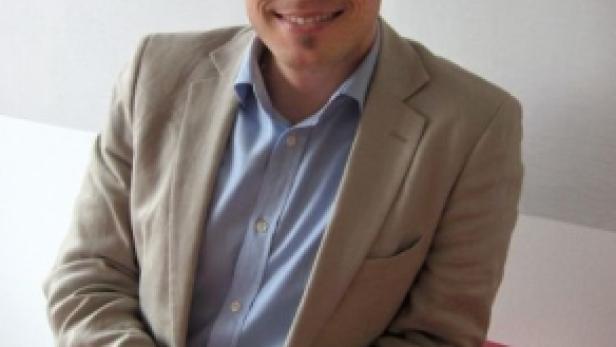 Ein Mann mit Brille und hellem Sakko lächelt in die Kamera.