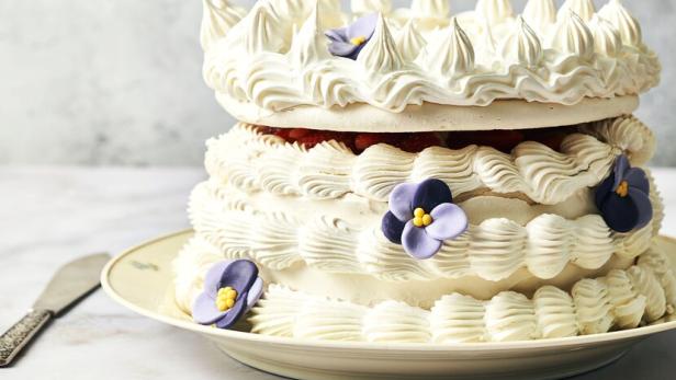 Eine zweistöckige Torte mit weißer Creme und lila Blüten auf einem Teller.