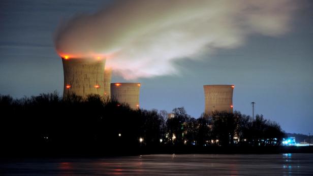 3 große Kühltürme eines Kraftwerks stoßen nachts dichte Dampfwolken aus, im Vordergrund sind Bäume.