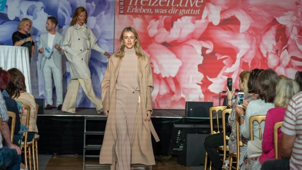 Eine blonde Frau präsentiert Mode auf einem Laufsteg vor Publikum.