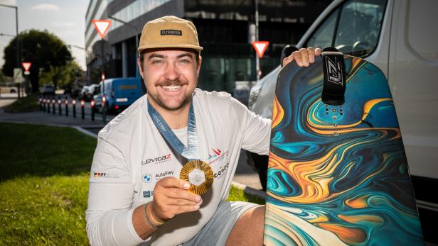 Olympiasieger Valentin Bontus vor seinem Bus mit Goldmedaille und Kitesurfbrett