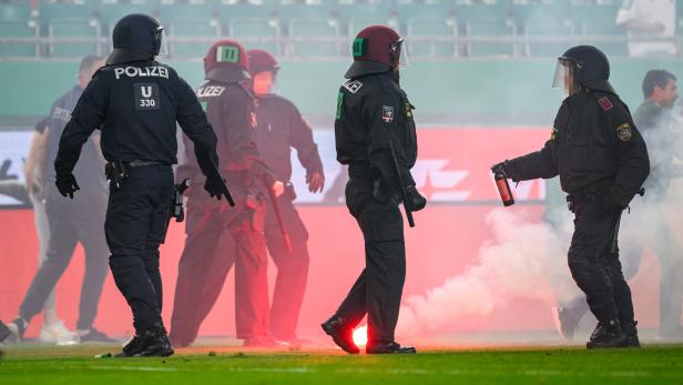 Polizisten in Schutzausrüstung stehen auf einem Fußballfeld inmitten von rotem Rauch.
