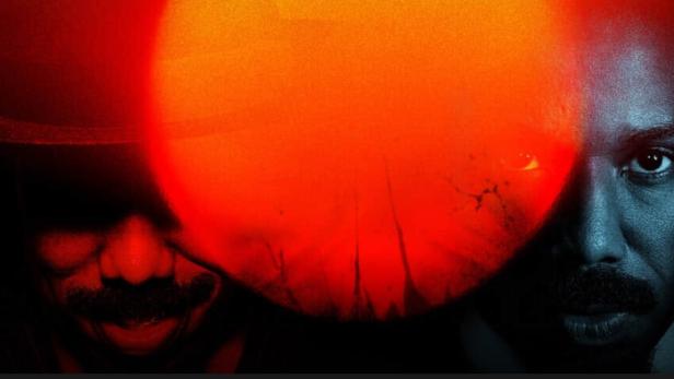 Ein Mann mit Schnurrbart, zur Hälfte im Schatten, vor einem roten Hintergrund.