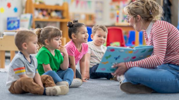 Eine Kindergartenpädagogin liest Kindern ein Buch vor.