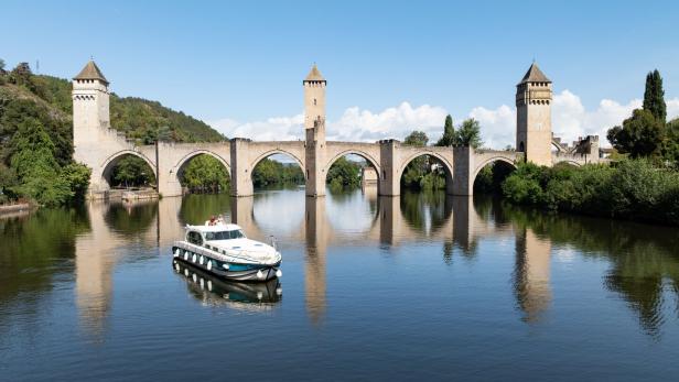 Eine Motorboot fährt unter dem Pont Valentré hindurch.