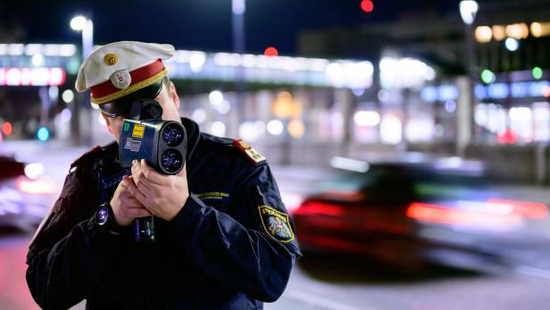 Ein Polizist misst mit einer Laserpistole die Geschwindigkeit eines vorbeifahrenden Autos.
