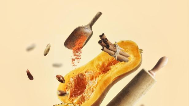 Ein Kürbiskuchen, Gewürze und Küchenutensilien schweben vor einem hellen Hintergrund.