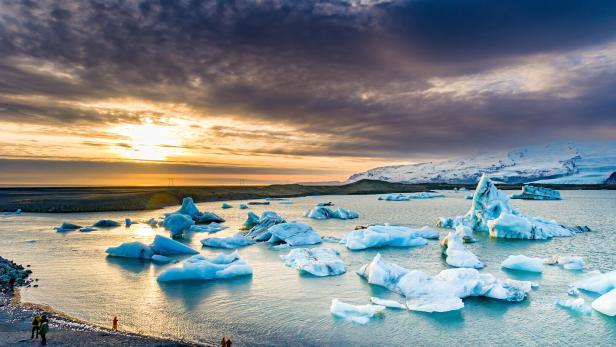 Menschen schauen auf Eisberge in einer Gletscherlagune auf Island bei Sonnenuntergang