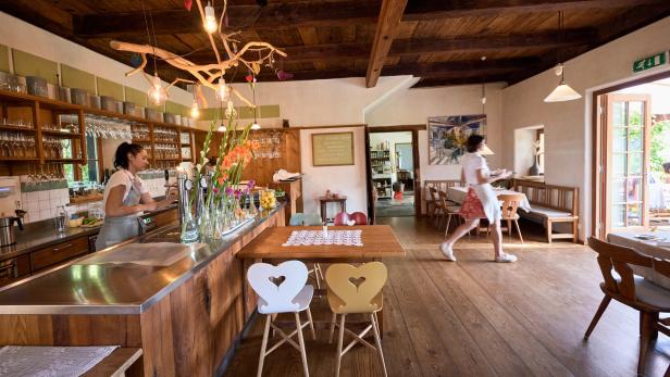 Innenansicht eines Restaurants mit einer Kellnerin an der Bar und einer weiteren, die ein Tablett trägt.