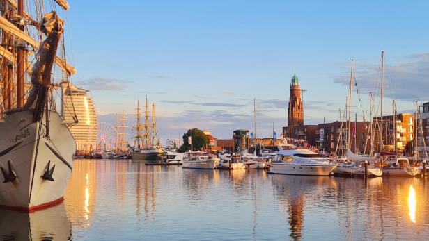 Ein Hafen voller Schiffe mit einem Riesenrad im Hintergrund im Sonnenuntergang.