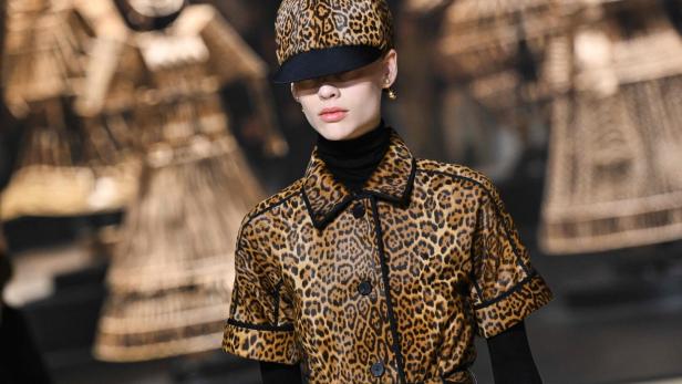 Ein Model trägt einen Mantel und eine Mütze mit Leopardenmuster auf dem Laufsteg.