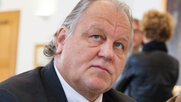 Porträt eines Mannes mit grauem Haar und einem dunklen Anzug.