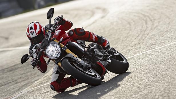 Ein Motorradfahrer in roter Lederkombi fährt eine Ducati auf einer Rennstrecke.