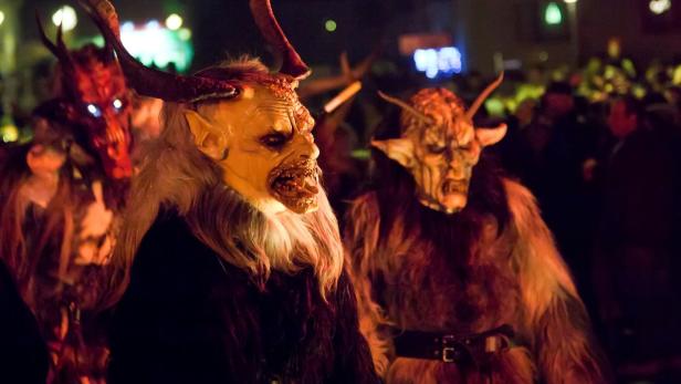 Drei Krampusse mit furchteinflößenden Masken und Hörnern stehen in einer Menschenmenge.