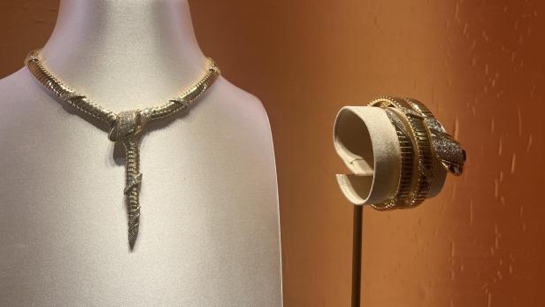 Eine goldene Schlangenhalskette und ein Armband auf Schmuckständern.