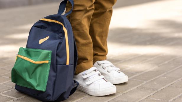 cropped shot of stylish schoolboy standing with backpack on street