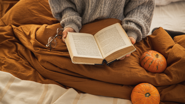 Eine Person liest ein Buch im Bett, neben ihr liegen zwei Kürbisse.