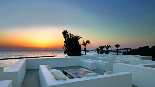Ein Dachgarten mit weißen Mauern und Blick auf das Meer bei Sonnenuntergang.