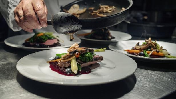 Ein Koch garniert Wild mit Gemüse und Pilzen auf Tellern.