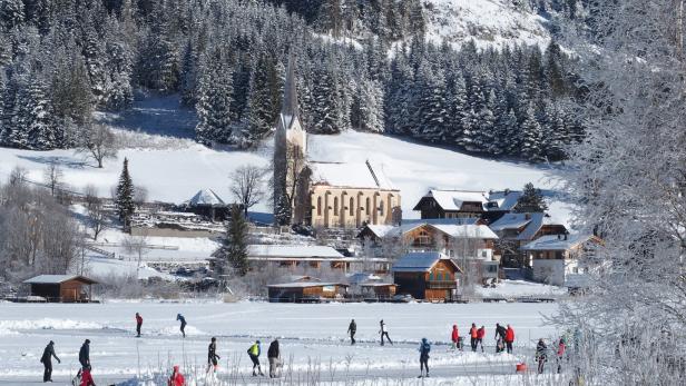 verschneite Landschaft am Weissensee in Kärnten, Eisläufer auf dem zugefrorenen See, Kirche im Hintergrund