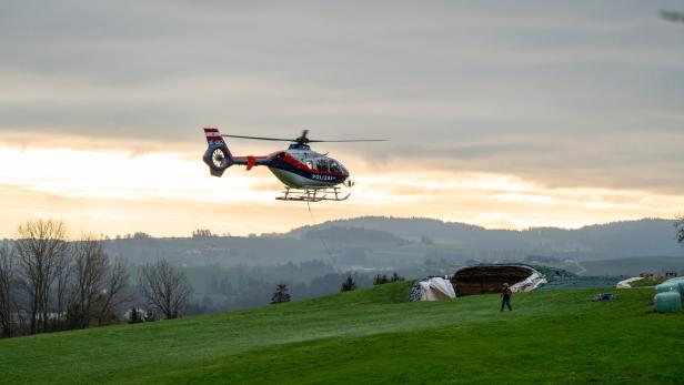 Ein Polizeihubschrauber schwebt über einer grünen Wiese, während eine Person am Boden ein Seil hält.