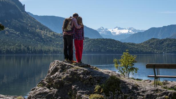 Ein Paar umarmt sich auf einem Felsen mit Blick auf einen See und Berge.