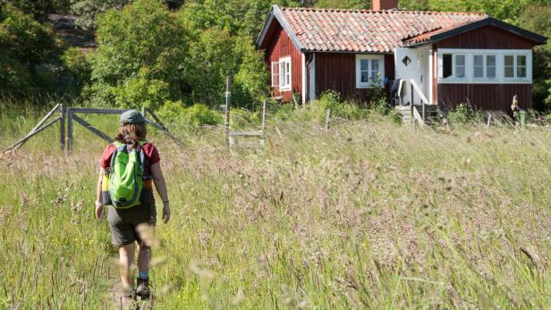 Frau beim Wandern auf den schwedischen Schären vor typisch schwedischem roten Haus