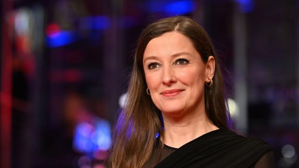 Alexandra Maria Lara mit braunen Haaren und Ohrringen lächelt vor einem verschwommenen Hintergrund.