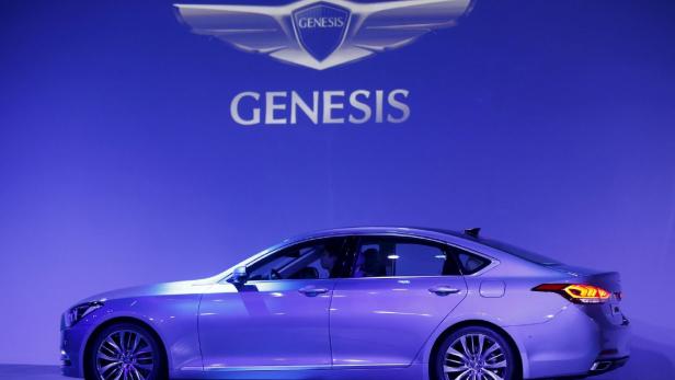 Ein silberner Genesis steht vor einem blauen Hintergrund mit dem Genesis-Logo.
