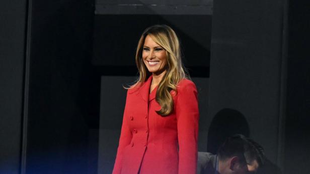 Melania Trump in einem roten Hosenanzug lächelt.