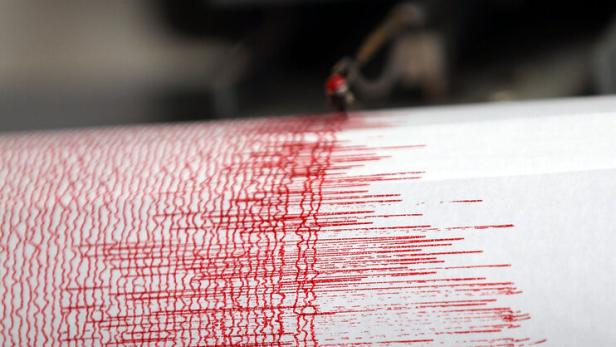 Ein Seismograph zeichnet mit einer roten Nadel starke Ausschläge auf weißem Papier auf.