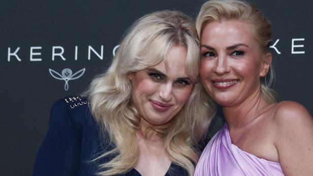 Rebel Wilson und Ehefrau Ramona Agruma lächeln vor einem dunklen Hintergrund mit dem Schriftzug "KERING".