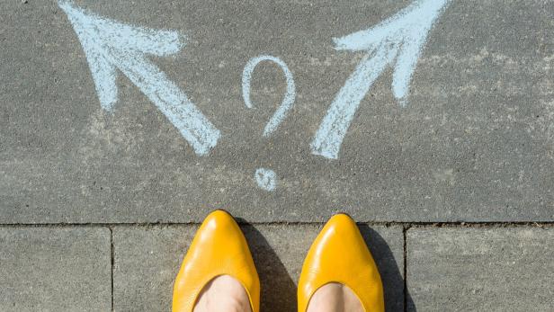 Gelbe Schuhe vor einem Fragezeichen und zwei Pfeilen auf dem Boden.