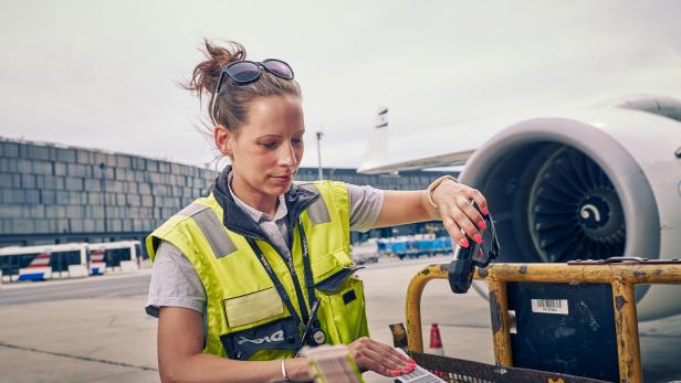 Mitarbeiterin des Flughafen Wien scannt Gepäck-Label vor einem Flugzeug