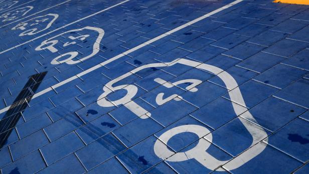 Blaue Parkplätze mit weißen Symbolen für Elektroautos und gelben Radstoppern.