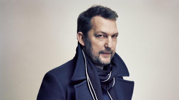 Ein Mann mit Bart und Mantel posiert mit einer Hand in der Hosentasche.