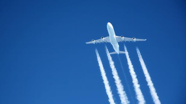 Ein Flugzeug zieht Kondensstreifen vor einem blauen Himmel hinter sich her.