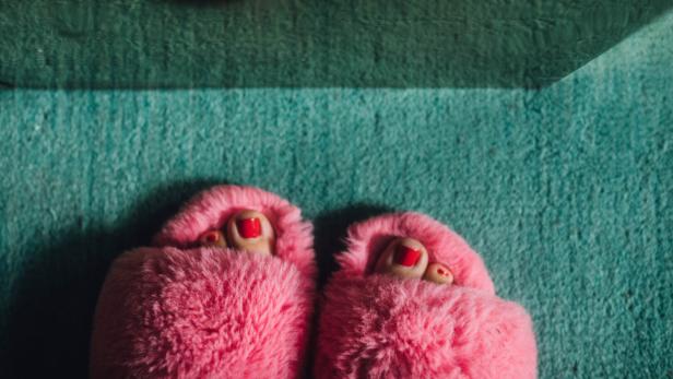 Füße in pinken Pantoffeln auf einem türkisfarbenen Teppich.