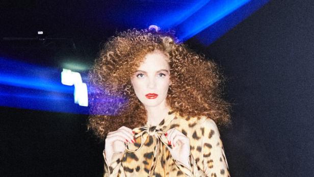 Eine Frau mit lockigem Haar trägt ein Kleid von Oscar de la Renta bei Popp & Kretschmer.