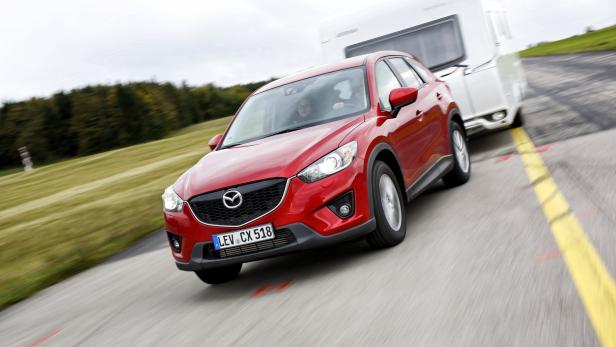 Ein roter Mazda CX-5 zieht einen weißen Wohnwagen auf einer Straße.